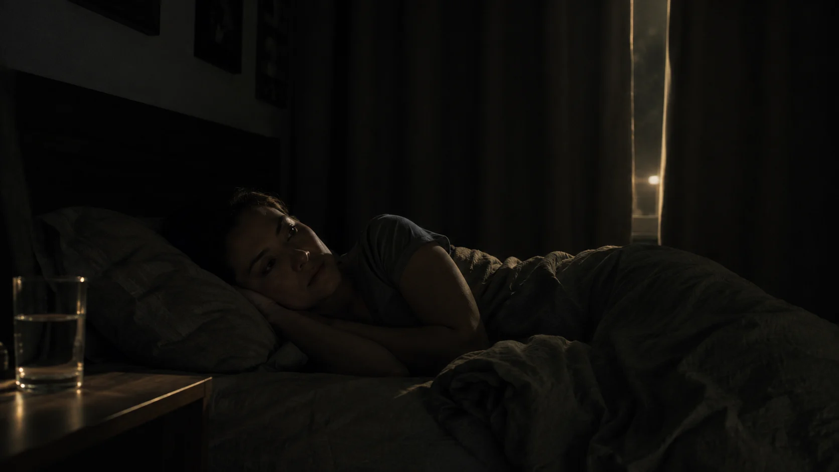 Woman lying awake in bed, eyes open, glass of water on nightstand