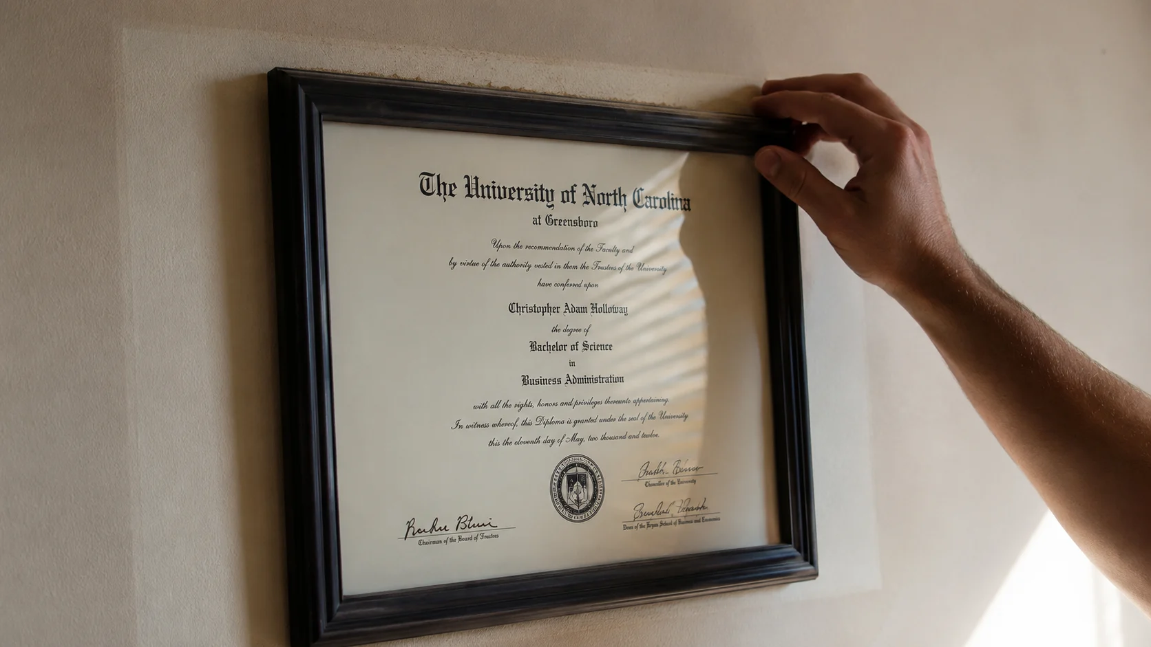 Hand straightening a dusty framed certificate on a sun-faded wall